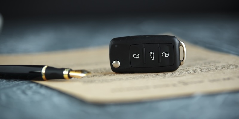 A black car key and pen sit on top of vehicle paperwork.